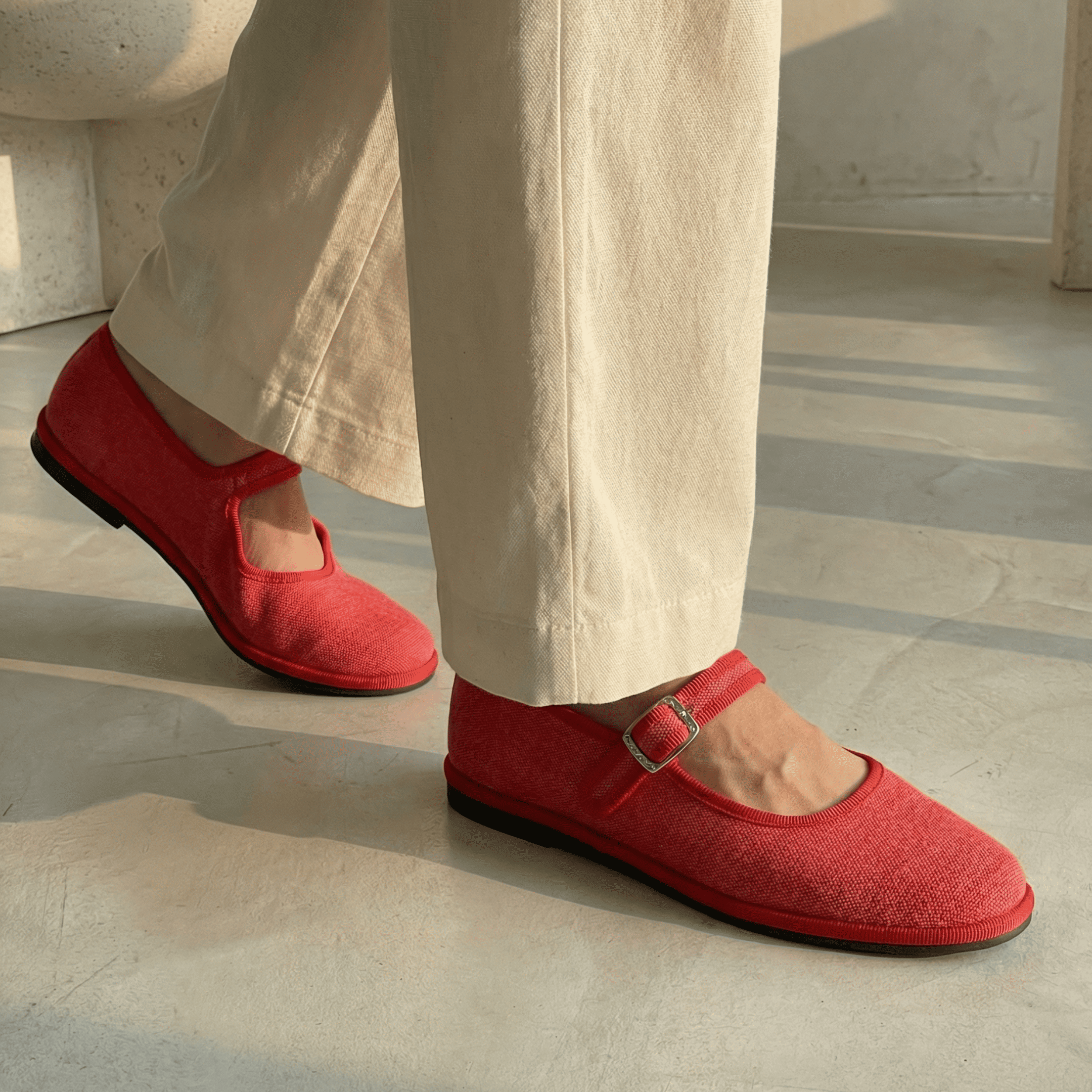 Red shoes worn with beige pants on a light wooden floor.