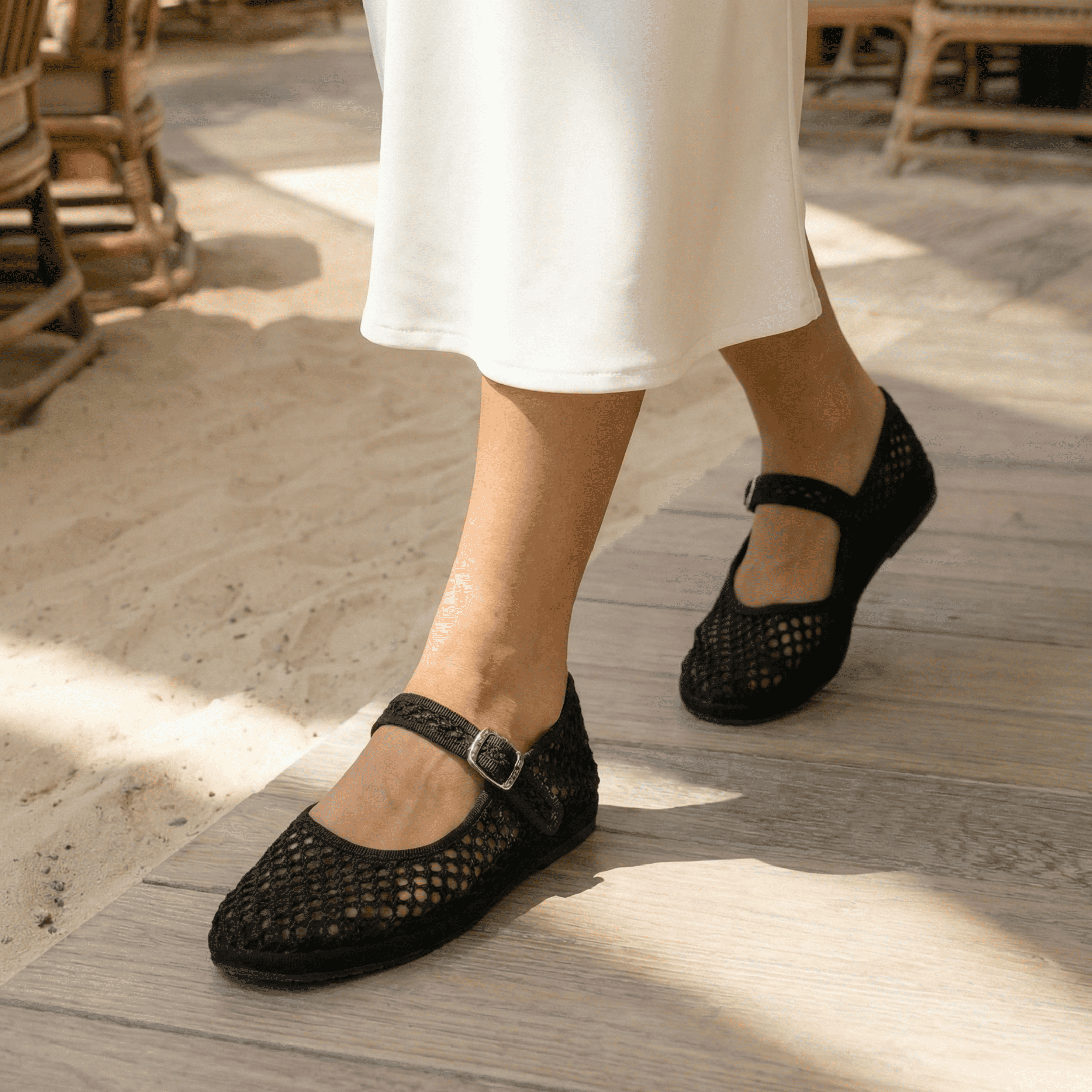 Black woven shoes worn with white pants on a wooden floor.